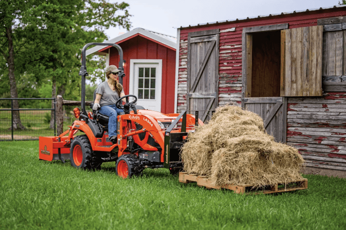 Woman moving a pallet of hay stacks with tractor