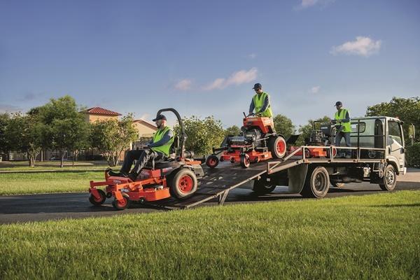 Landscaping crew driving mowers off the back of trailer