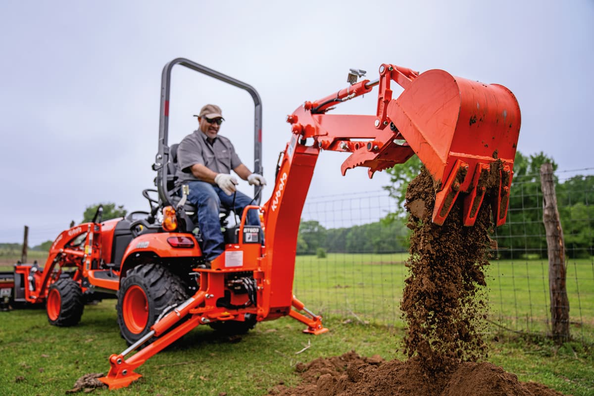 A man operating rear backhoe on tractor